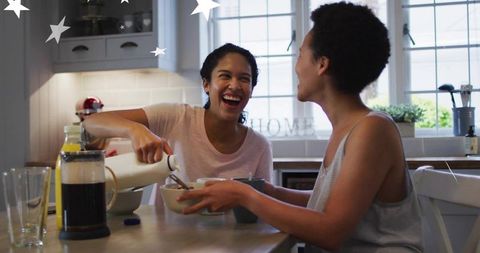 Friends laughing, pouring milk, sharing cozy morning breakfast at sunlit kitchen table