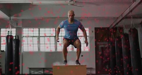 Explosive box jump training by male athlete in industrial gym with chalk dust and heavy bags