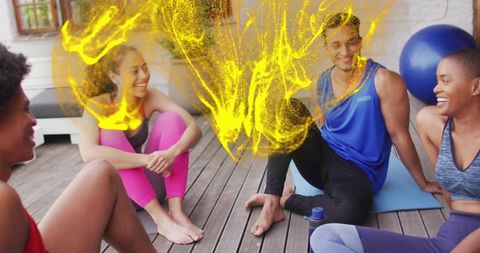 Friends laughing during outdoor group yoga session on wooden deck with yellow energy burst