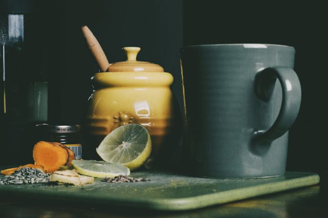 Close-up scene of preparing a healthy morning tea with honey, lemon, ginger, and turmeric. The honey jar has a dipper, and a grey mug is ready for pouring. Ideal for lifestyle blogs, recipes, wellness articles, or kitchen décor inspiration.