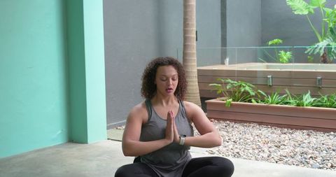 African american woman meditating on patio by teal column wearing gray tank and smartwatch