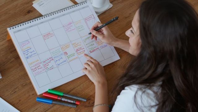Woman writing color-coded spiral monthly planner with markers for productivity and planning