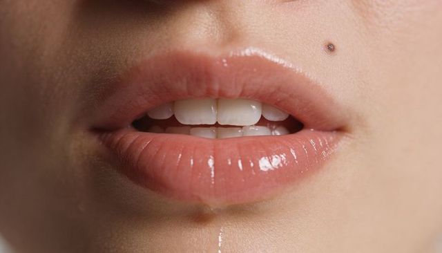 Showing glossy slightly parted lips with droplet and mole, close-up beauty detail