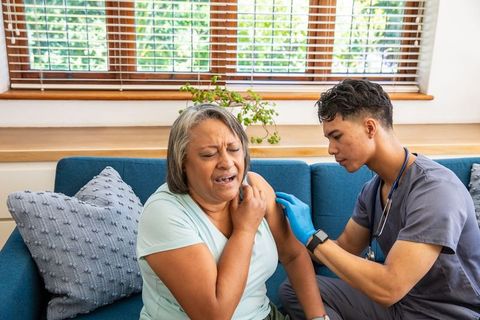Senior woman wincing as caregiver administers injection on couch