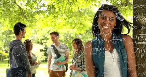 Smiling college student leaning on tree with friends and chemistry doodles overlay