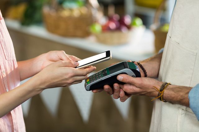 Woman using smartphone to make a contactless payment via NFC technology at a retail store. Ideal for illustrating modern payment methods, digital wallets, and the convenience of mobile transactions in retail environments.