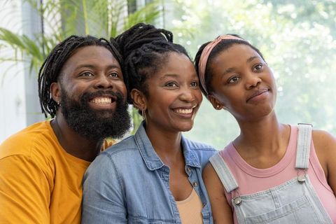 Sunlit black family portrait with smiling parents and teen daughter in cozy sunroom