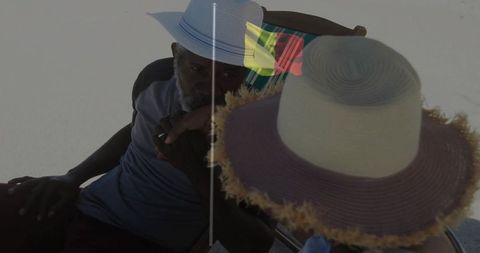 Men talking on sunlit beach wearing fedora and wide-brim straw hat, relaxing