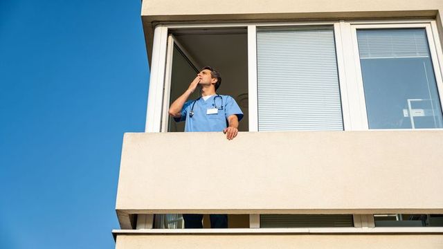 Medical professional on balcony taking reflective break in blue scrubs with stethoscope