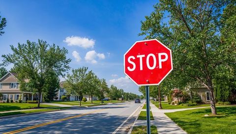 Red Octagonal Stop Sign Marking Sunny Tree-Lined Suburban Street with Sidewalk