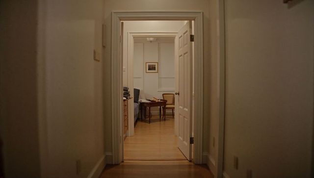 Partially open white door framing cozy bedroom with wooden table chair and ambient light