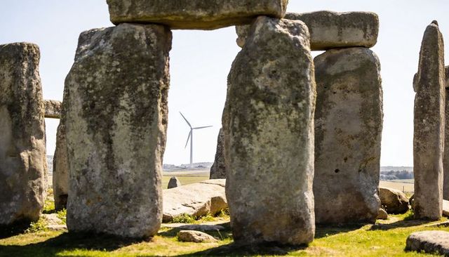 Megalithic trilithon framing distant wind turbine on rolling rural heritage landscape