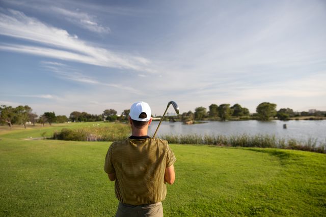 Rear view of Caucasian male golfer practicing on a golf course on a sunny day wearing a cap and golf clothes, holding a golf club on his shoulder. Hobby healthy lifestyle leisure.