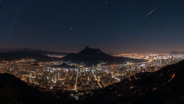 Nighttime urban panorama showing mountain silhouette, glowing bay lights and starry sky