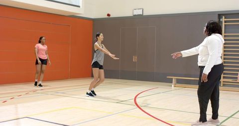 Women athletes training in gymnasium group drill with coach guiding jump exercise technique