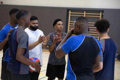 Teen volleyball team huddling, clapping and listening to asian coach in indoor gymnasium