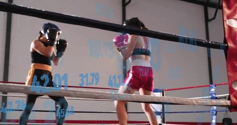 Female boxers sparring in ring with blue data graphics, pink gloves, intense training