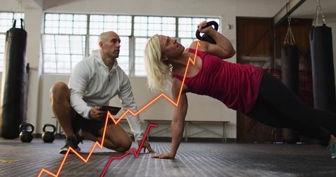 Female athlete holding kettlebell in side plank while trainer monitoring fitness data