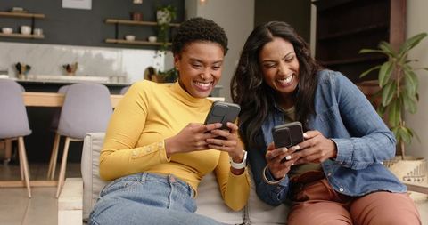 Diverse Women Joyfully Using Smartphones in Modern Living Room