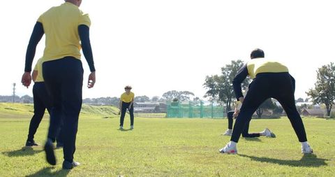 Male team practicing on sunny grass field wearing yellow training shirts and black pants