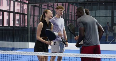 Energetic Group Playing Padel on Glass Court Expressing Friendship
