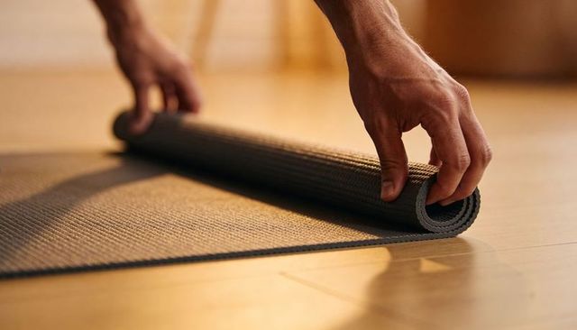 Rolling hands winding charcoal yoga mat on wood floor in warm morning light