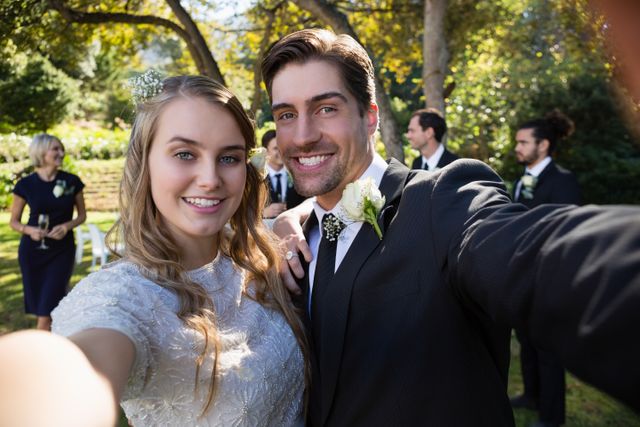 This image captures a joyful couple posing together in a park during their wedding. The bride and groom are smiling and dressed in formal attire, with the natural beauty of the park providing a picturesque backdrop. This image is perfect for use in wedding invitations, celebration announcements, or articles about weddings and outdoor ceremonies.