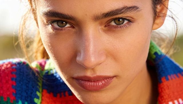 Gazing woman in colorful knitted sweater closeup portrait with intense eye contact outdoor meadow
