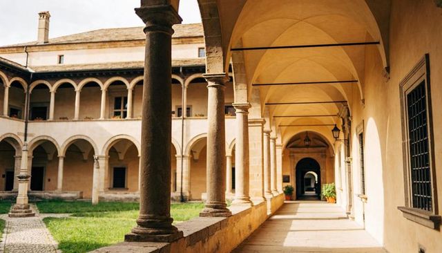 Basking sunlit cloister corridor featuring arched vaults, stone columns and courtyard