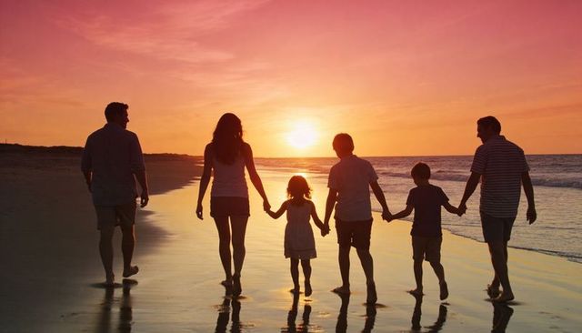 Family of six walking hand-in-hand at sunset on beach with reflective wet sand