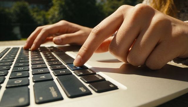 Close-up of hands typing on laptop keyboard outdoors, fingers pressing key for remote work