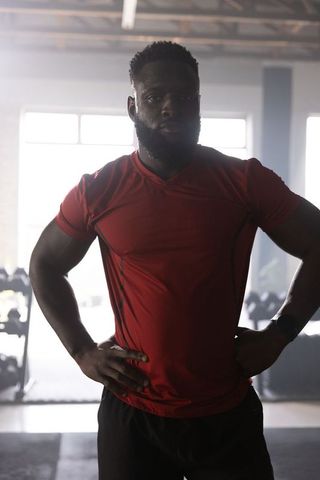 Backlit african american athlete standing hands on hips wearing red shirt in gym