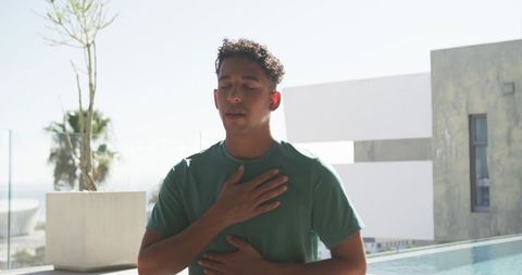 Young man practicing deep breathing on rooftop terrace by pool with ocean view
