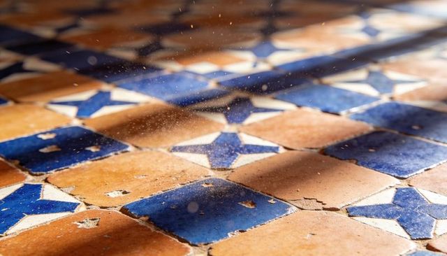 Sunlit weathered terracotta tiles with blue star motifs and dust motes in historic interior