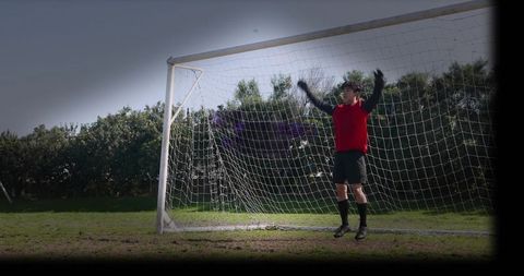 Goalkeeper jumping to save goal on muddy soccer pitch with ample copy space