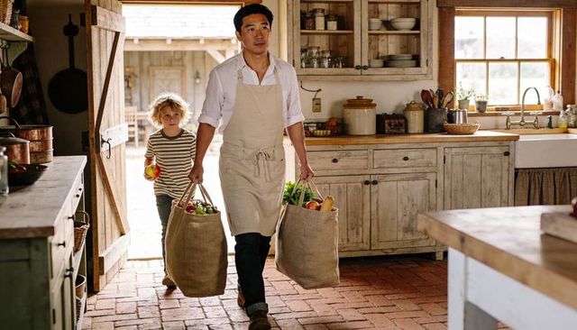Carrying burlap bags of fresh produce entering sunlit farmhouse kitchen with child