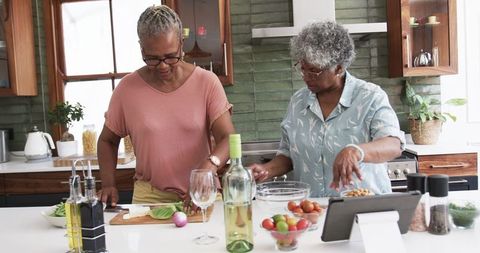 Senior Women Cooking Together in Modern Kitchen, Using Tablet Technology