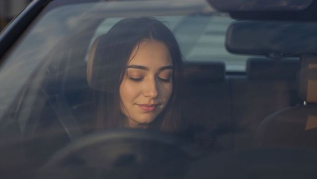 Young woman resting with closed eyes in car driver's seat during golden hour calm portrait