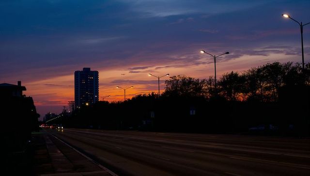 Empty city avenue stretching toward colorful sunset with glowing streetlights and distant tower