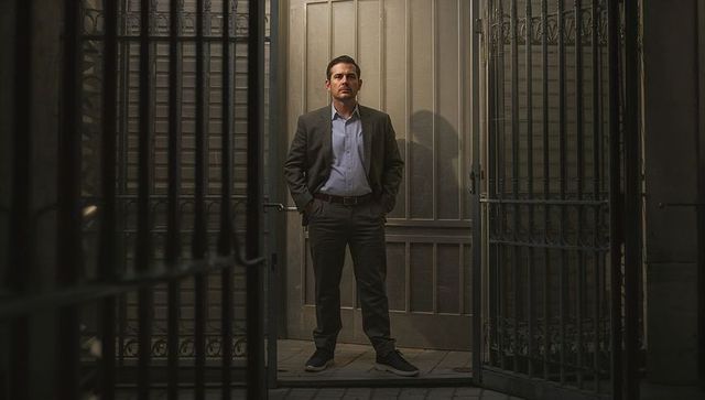 Standing Businessman Framed by Ornate Iron Gates and Panel Door Casting Dramatic Shadow