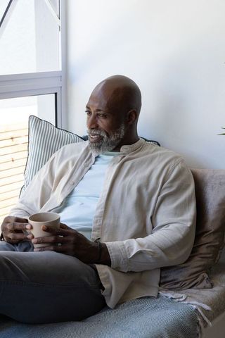 Mature african man relaxing on sofa with ceramic mug by window cozy morning interior