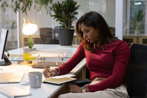 Indian woman writing notes at modern office desk, focusing on productivity and calm