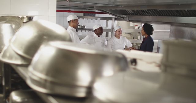 Four chefs in a professional kitchen engage in spirited discussion, highlighting teamwork and collaboration in a culinary setting. This image can be used for illustrating the dynamics of a restaurant kitchen, promoting culinary schools, or advertising kitchen equipment. It showcases the professional yet vibrant atmosphere of a working kitchen environment.