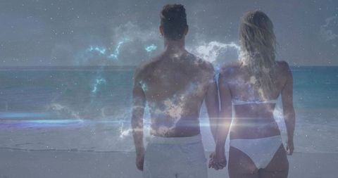 Holding hands couple watching ocean under starry nebula overlay with lens flare