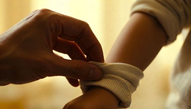 Parent rolling knit cuff on child wrist, warm intimate moment of care