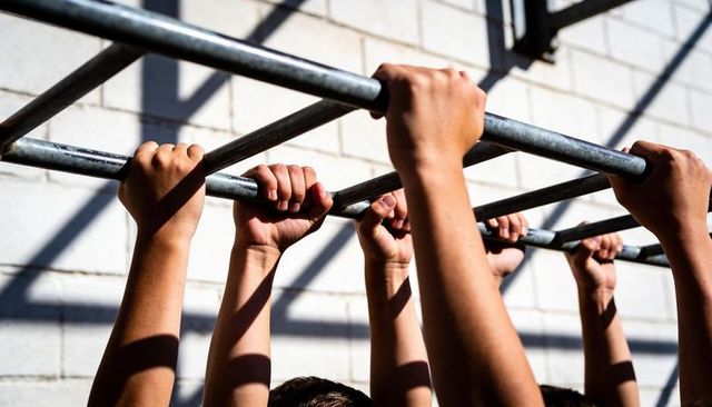 Teen hands gripping monkey bars under sunlight showing teamwork and playful strength