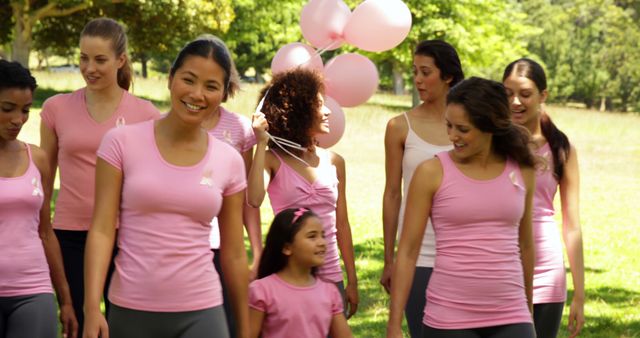 Women of various ethnicities, ages and body types smiling and walking outdoors in a park, all wearing pink shirts. Some women are holding pink balloons. This image can be used for topics related to breast cancer awareness, charity walks, community events, health, fitness, and group activities.