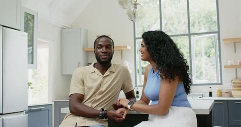 Multicultural couple holding hands on bright modern kitchen island wearing smartwatches