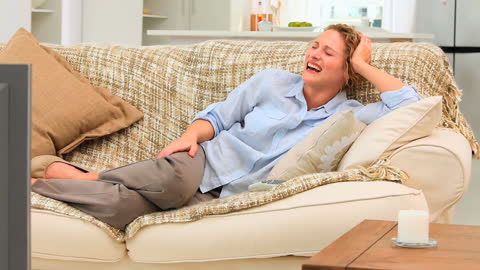 Smiling Woman Relaxing on Couch Enjoying TV at Home