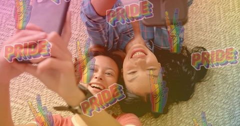 Friends taking pride selfie lying on rug smiling in plaid and coral tops with rainbow stickers